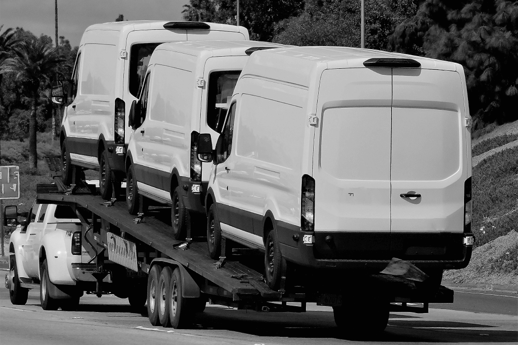 Vans on a flatbed trailer on the highway.
