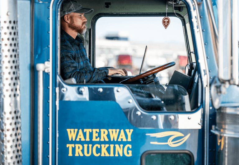 a seated man in the driver seat viewed through the passenger window of a truck