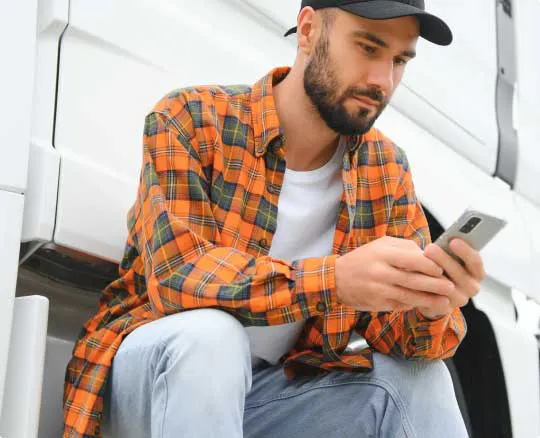 Carrier sitting by a truck using Shipper Hub on a phone