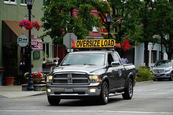 Escort pickup truck with oversize load sign and safety flags used to guide heavy haul or oversized freight.
