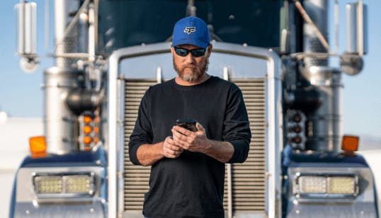 Carrier standing by truck using cellphone.