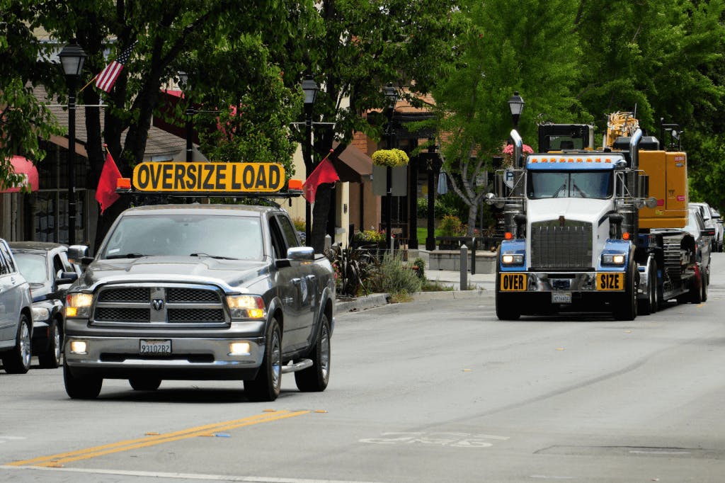 oversized load guide car in front of truck on road