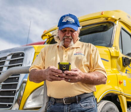 Ernie Hall, a Truckstop customer, using the load board app to find loads for his yellow dry van, which is behind him.