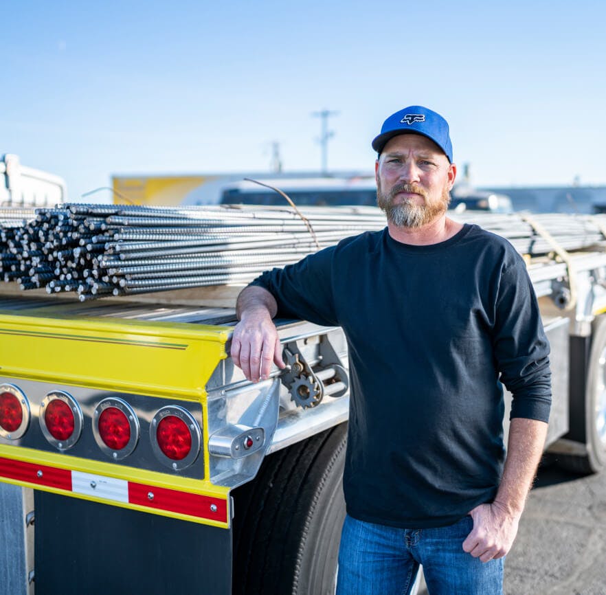 Carrier standing in front of his flatbed trailer loaded with rebar.
