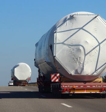 Two heavy haulers carrying large heavy cylinders driving down a freeway.