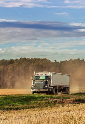 a semi truck carrying grain drives through a field