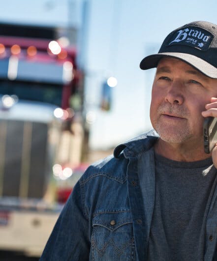 carrier talks on the phone and looks into the distance with his truck visible in the background