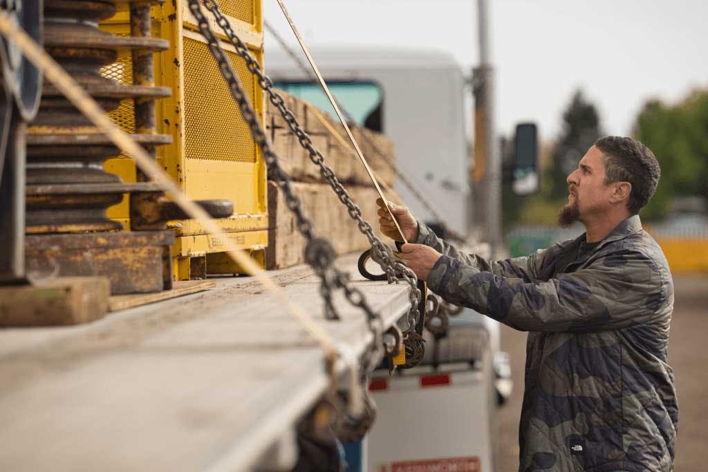 Carrier checking straps on a flatbed load.
