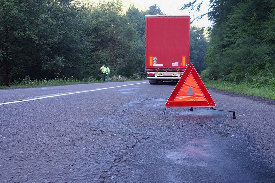 THe back of a trailer with a hazard trianlgle on the asphalt.
