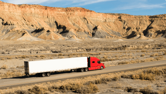 Red semi truck with white trailer against clifs
